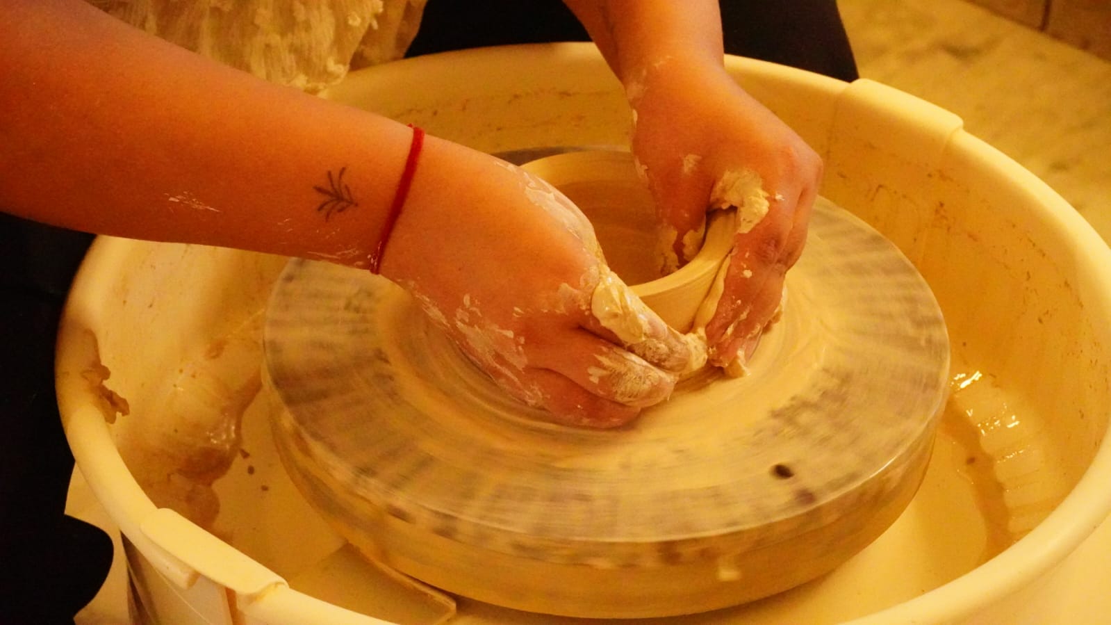 Clay-covered hands shaping a form on the pottery wheel